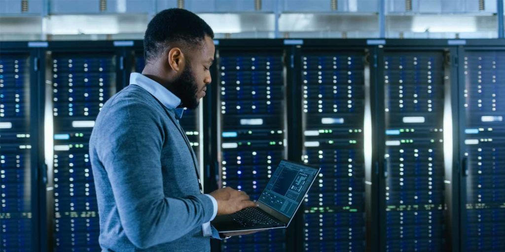 Man with laptop looking at data in front of servers