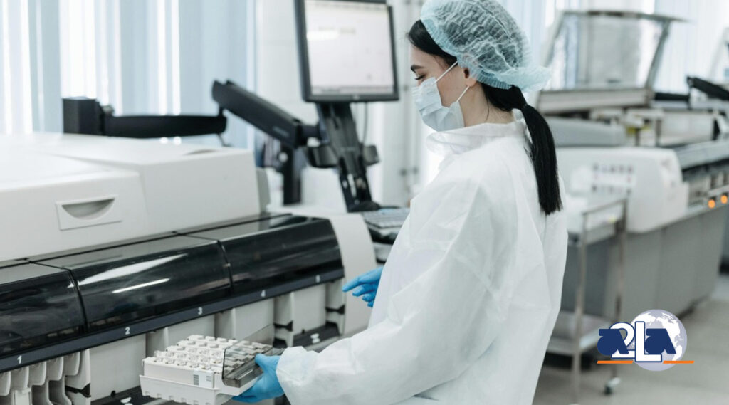 Woman in a lab coat, gloves, mask, and hair net places samples into a machine